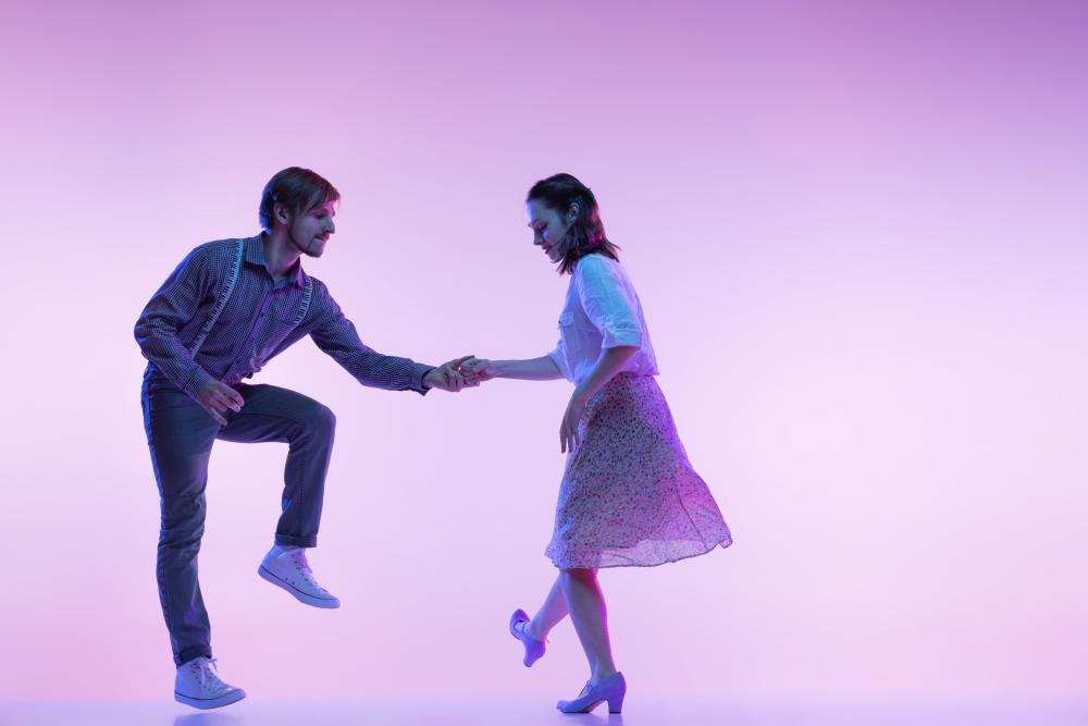two-young-people-man-and-woman-dancing-swing-isolated-over-purple-wall-in-neon-min